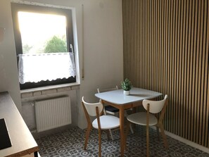 Pieni huone, jossa on ikkuna, patteri, pöytä tuoleineen ja ruukussa oleva kasvi.