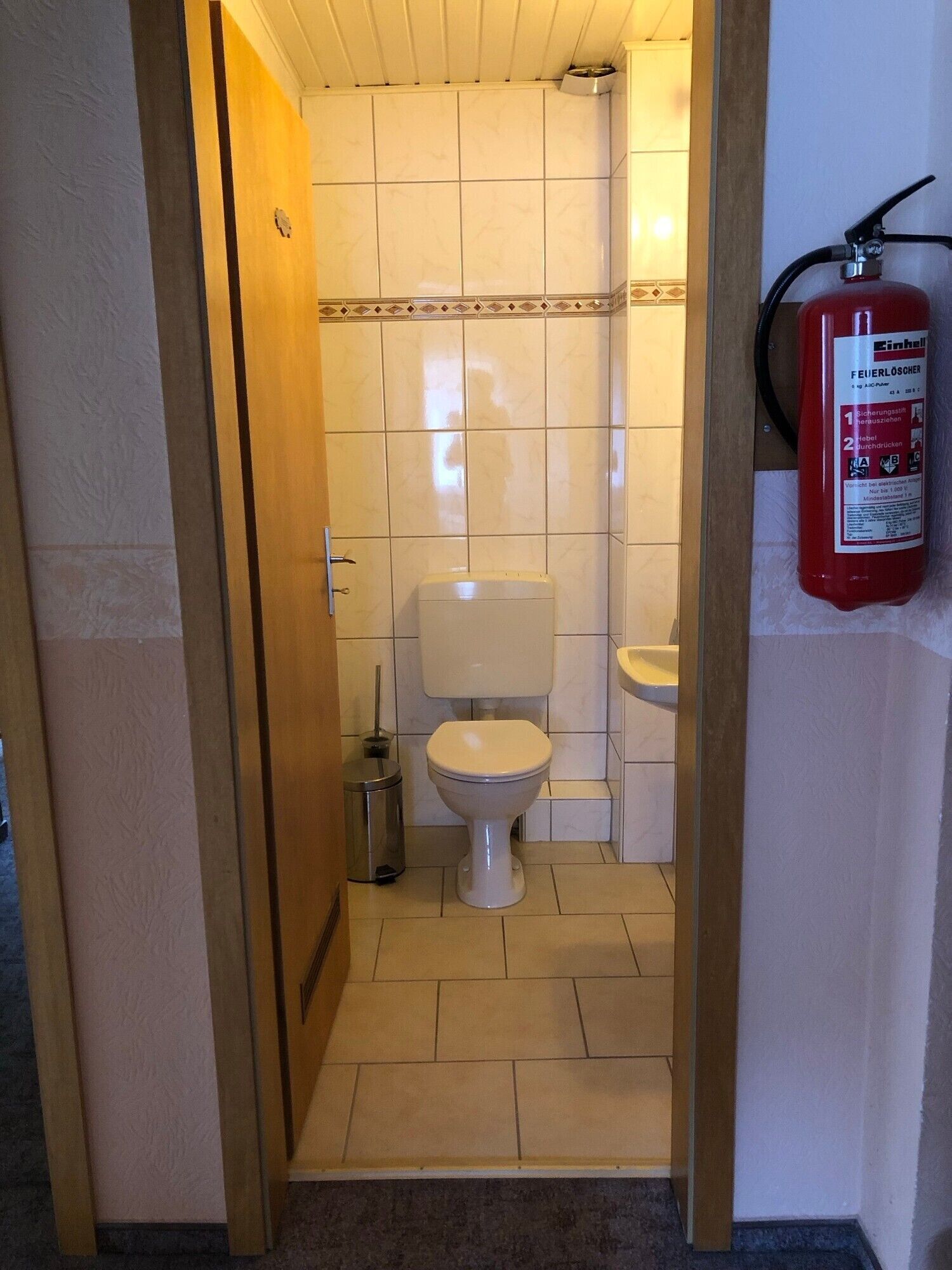 Un baño pequeño con inodoro, lavamanos y un extintor de incendios sujeto a la pared.