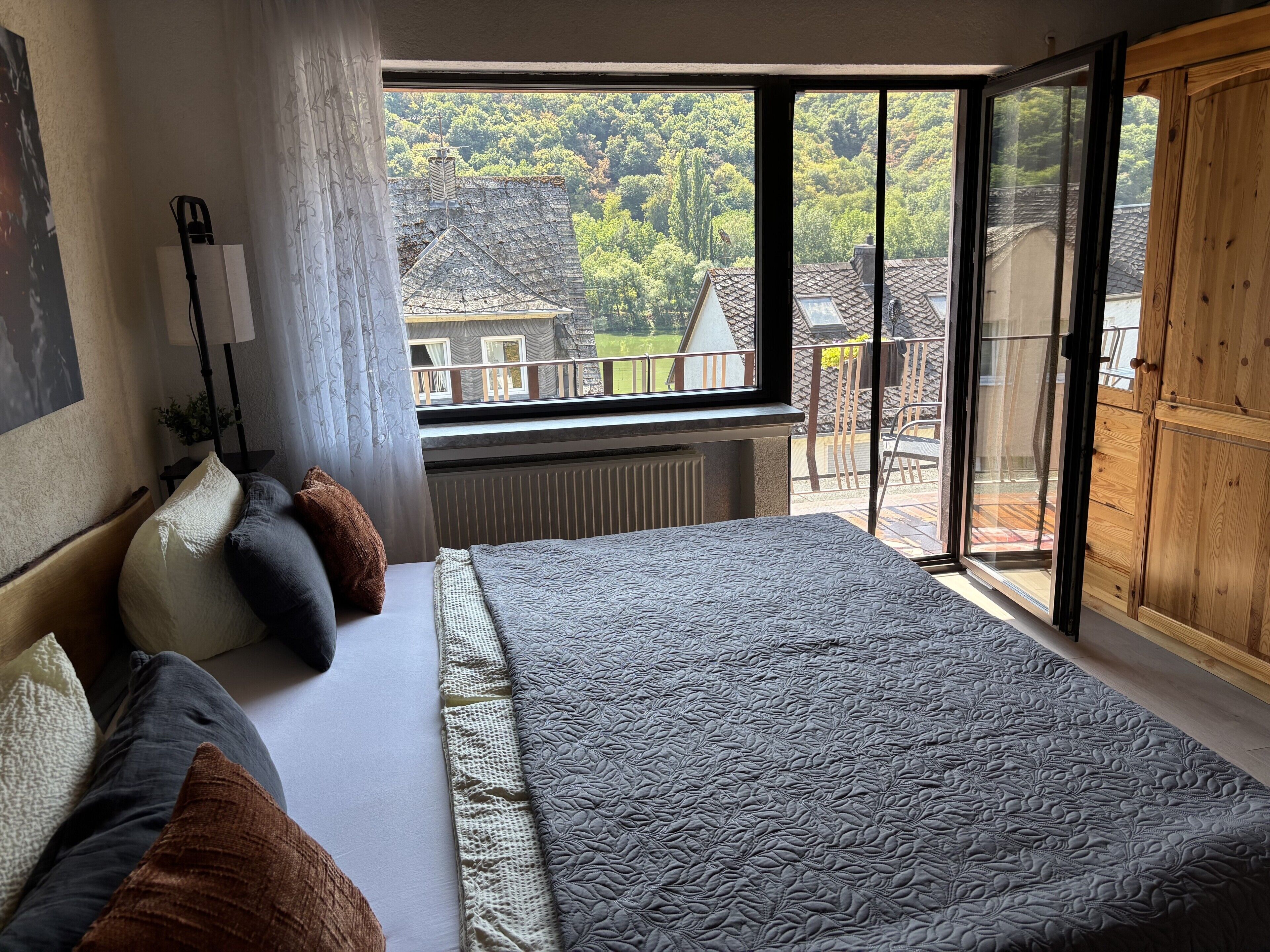 Ein Schlafzimmer mit einem großen Bett, einem Fenster mit Blick auf einen Wald und einer Holztür.