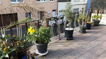 Ein Balkon mit Blumentöpfen, ein weißes Auto und ein Gebäude im Hintergrund.