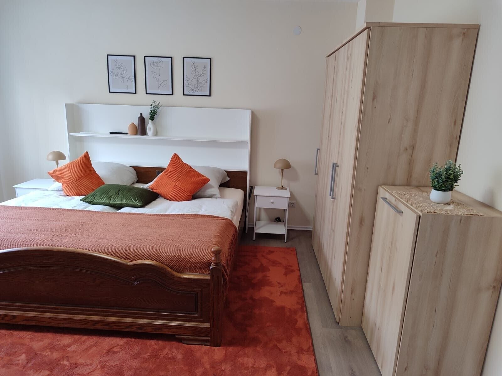 Una camera da letto con un letto in legno, un comodino bianco, un armadio in legno e tre quadri appesi al muro.