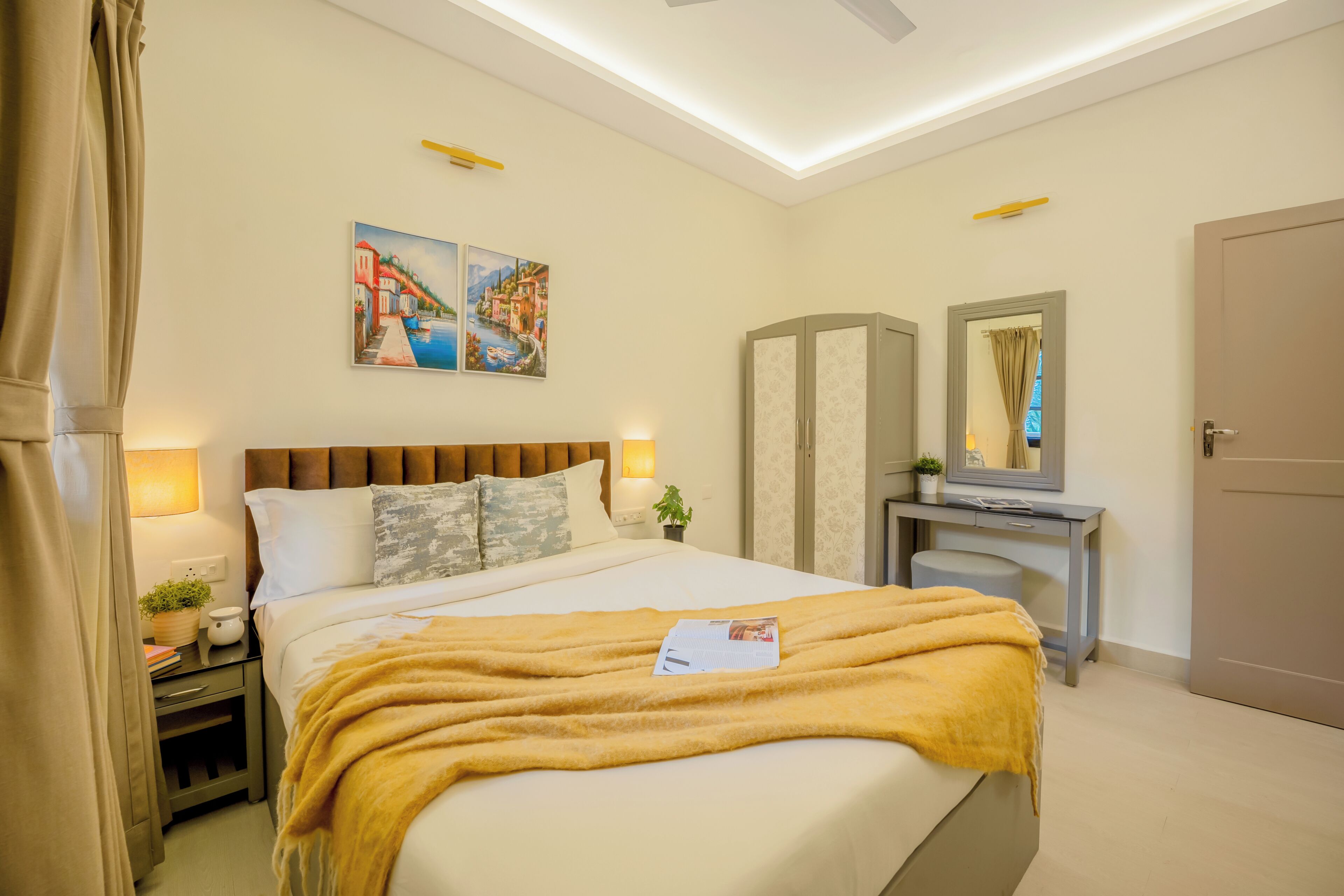 A hotel room with a bed, bedside table, lamp, nightstand, and a desk with a mirror.