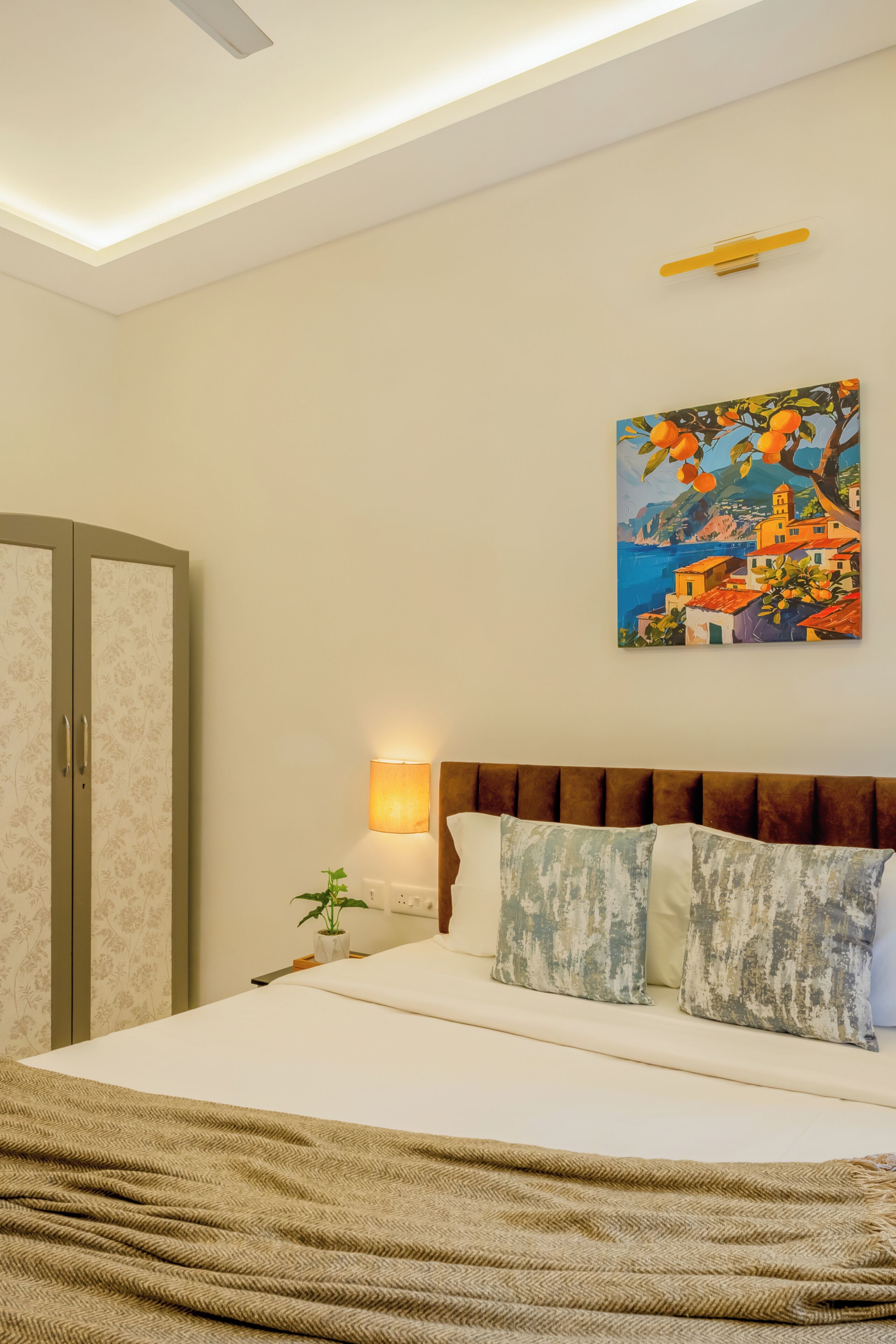 A bedroom with a bed, a nightstand, a lamp, a painting, and a wardrobe.