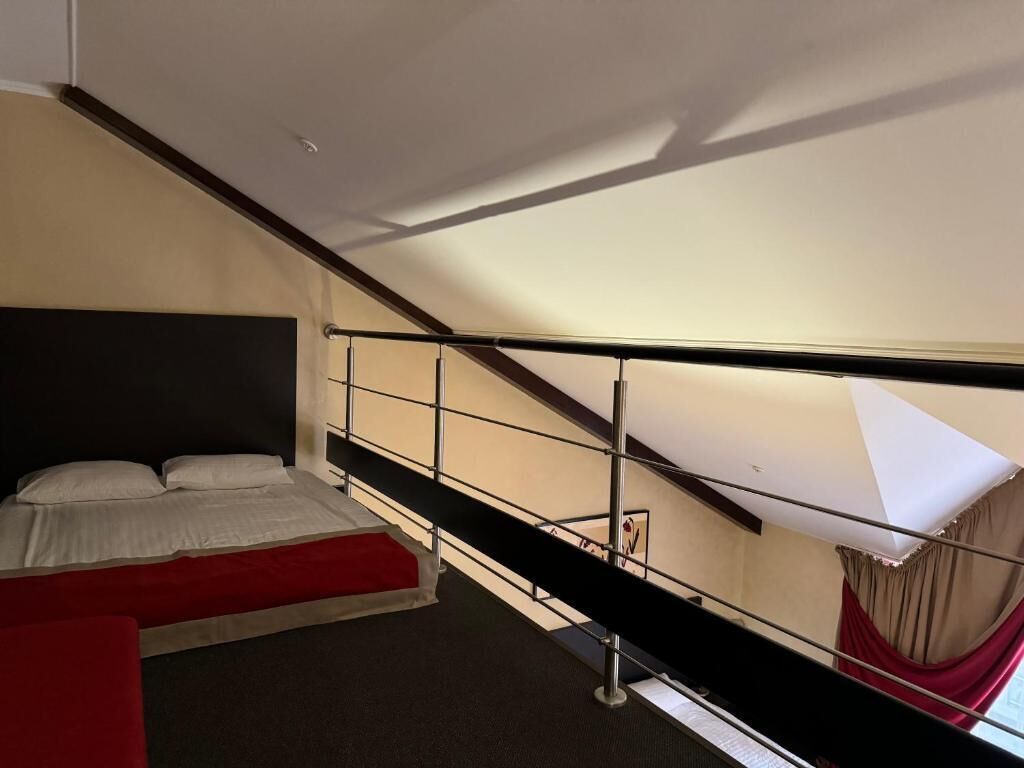 A bedroom with a bed, a red bench, a staircase, and a window with a curtain.