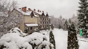 En stor bygning med mange vinduer og en balkon, omgivet af sneklædte træer og et snefyldt landskab.