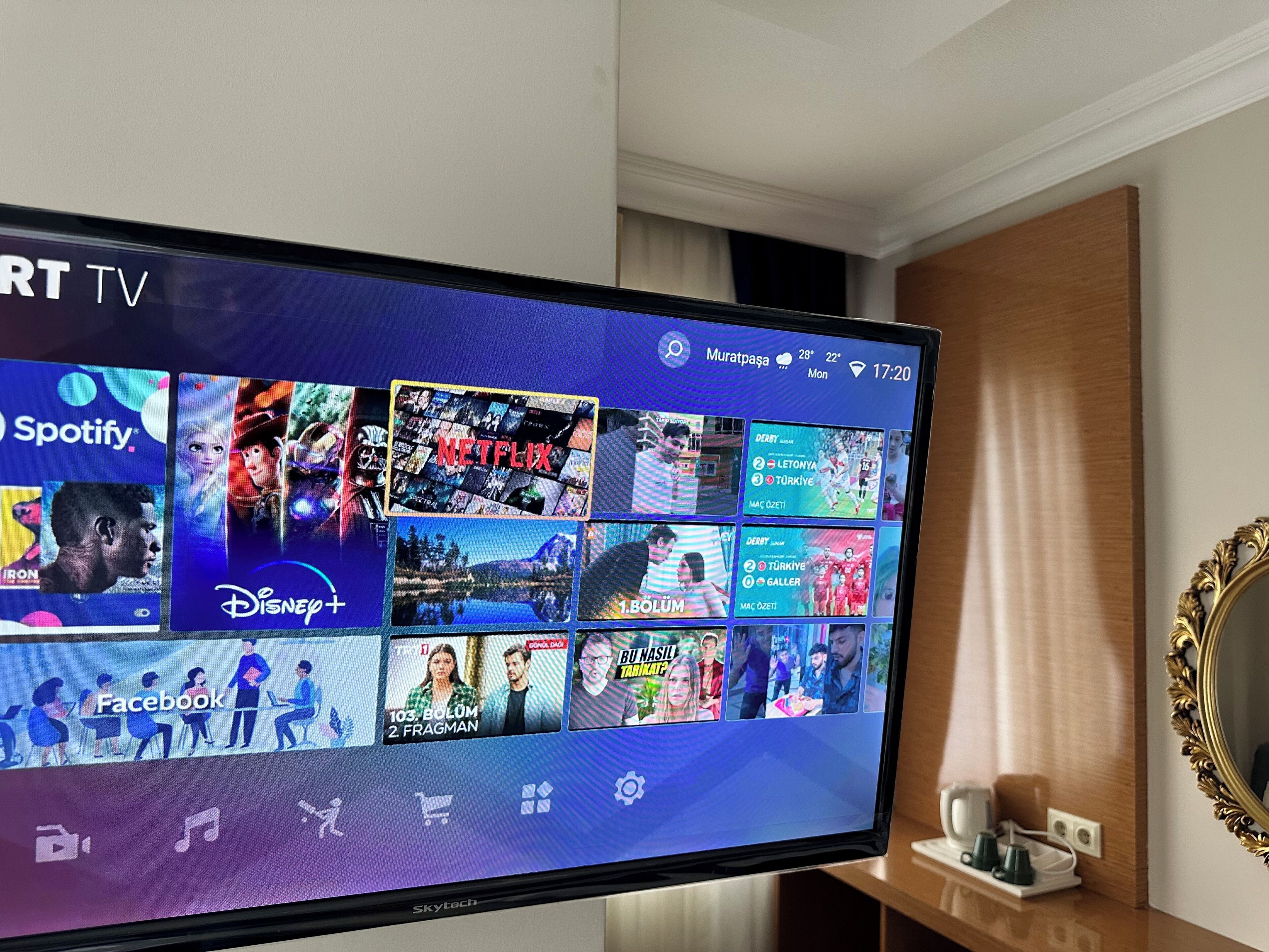 A TV screen displaying various streaming services and a room with a wooden cabinet and a mirror.