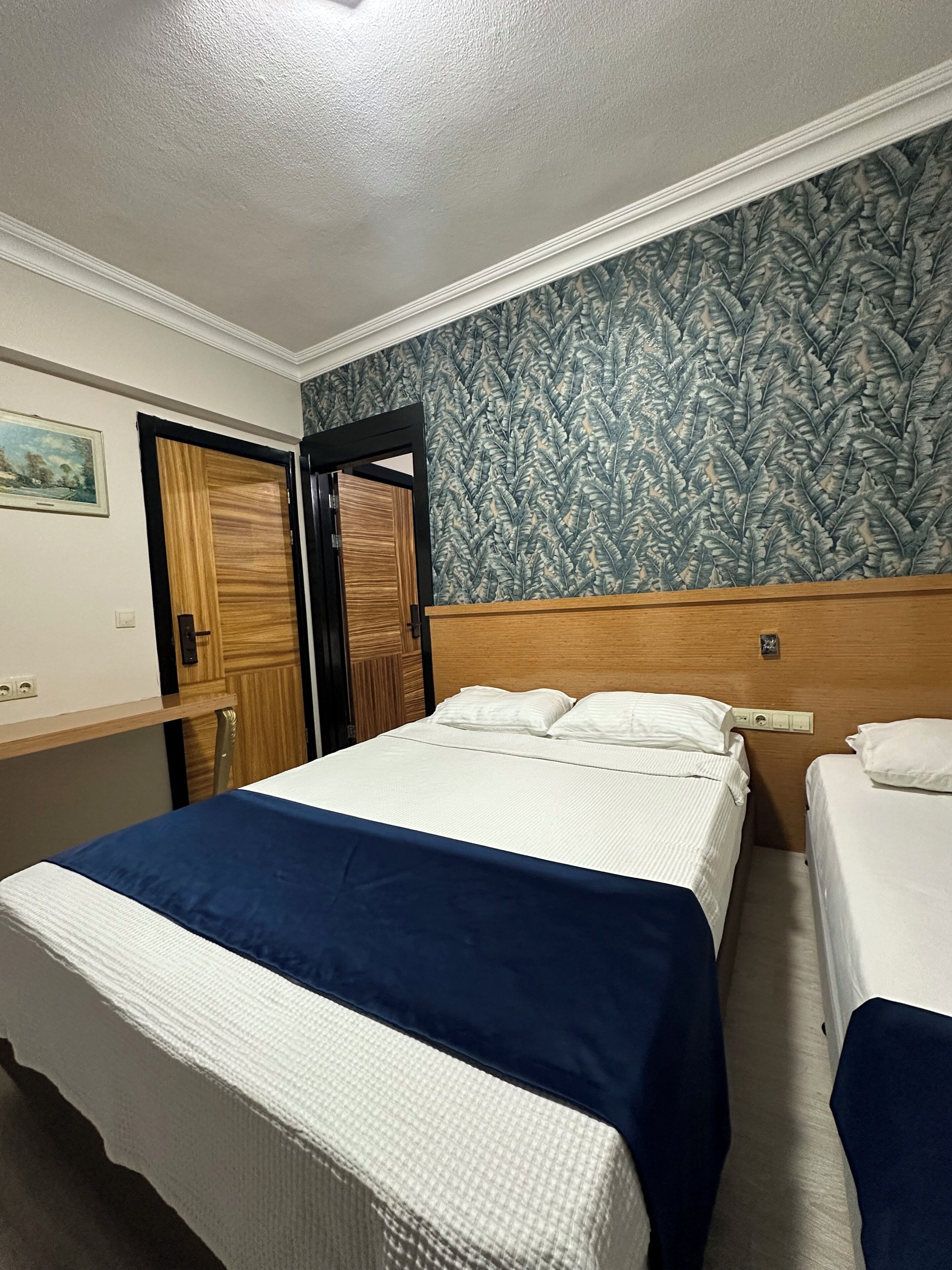Habitación de hotel con dos camas, cabecero de madera, papel tapiz estampado y un cuadro en la pared.