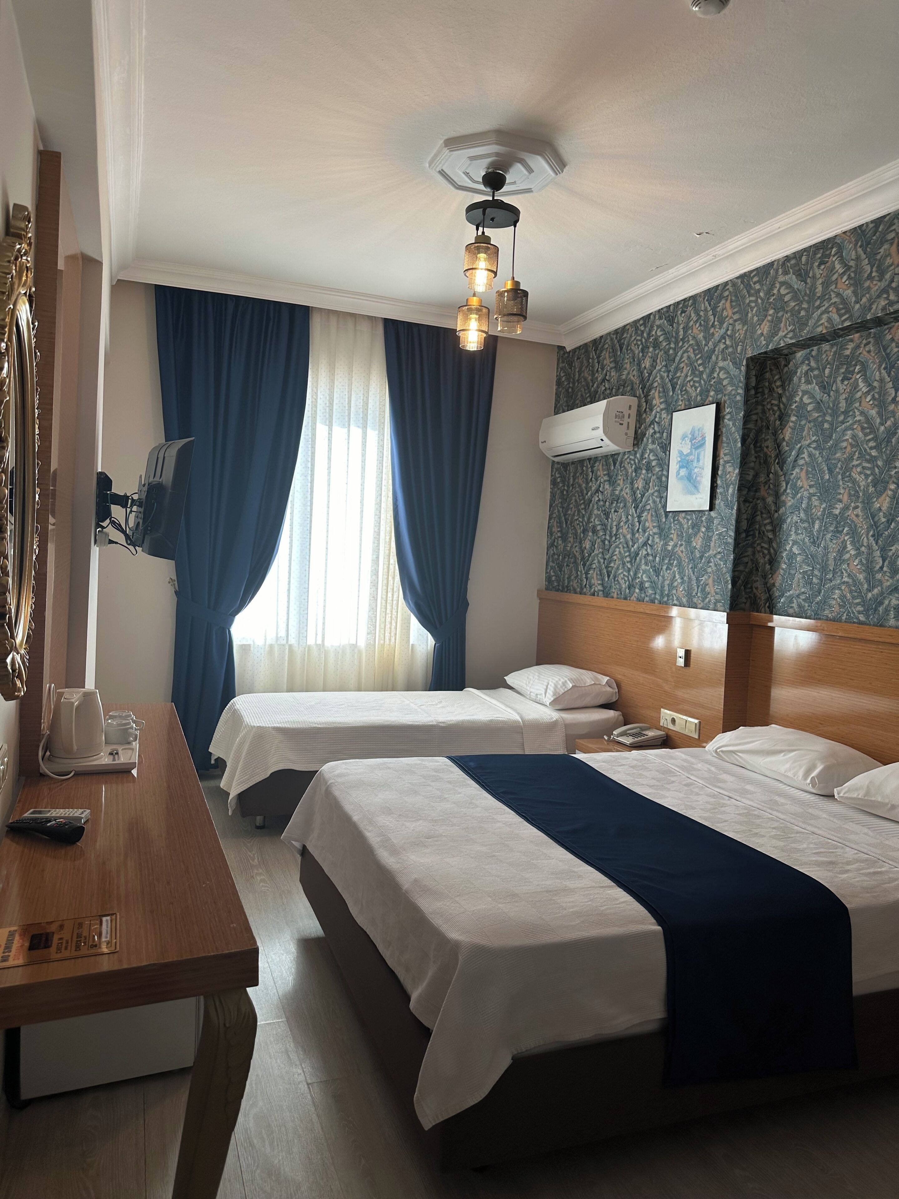 Une chambre d’hôtel avec deux lits, un bureau en bois, un téléphone et un climatiseur fixé au mur.