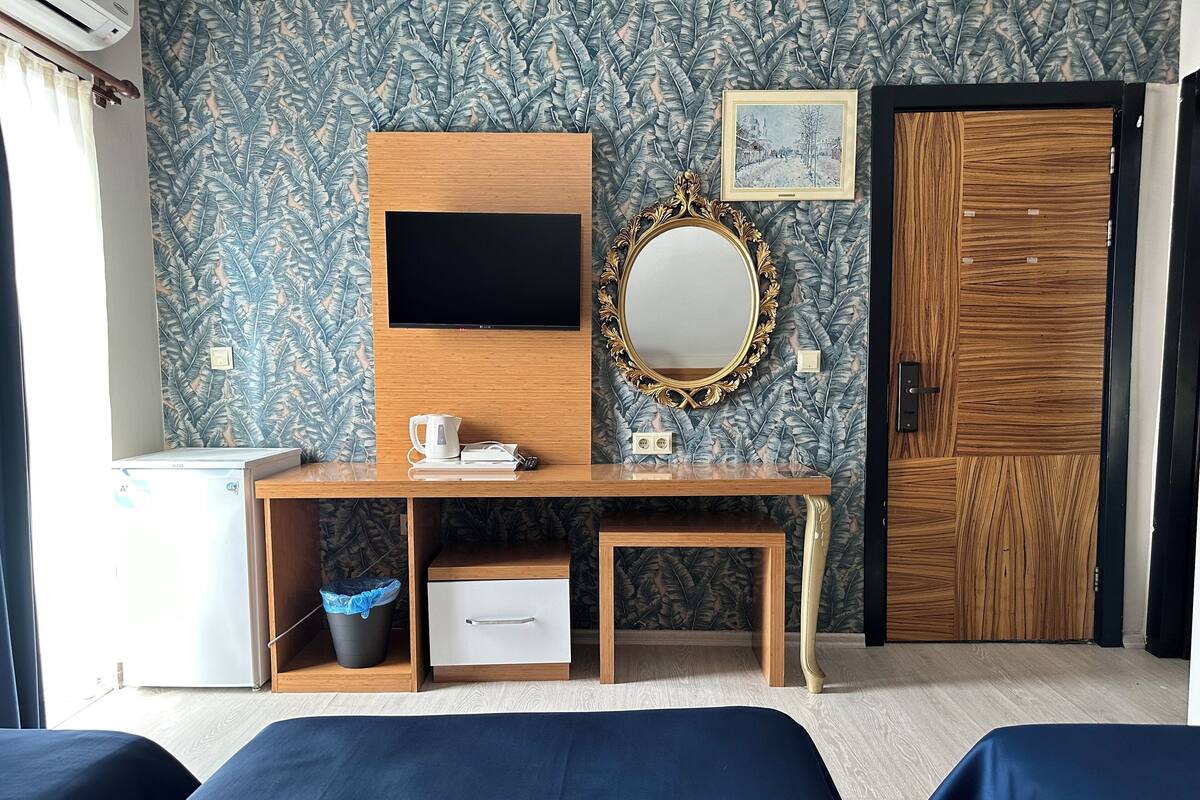 Une chambre d’hôtel avec un bureau en bois, une télévision, un miroir, une porte et deux lits.