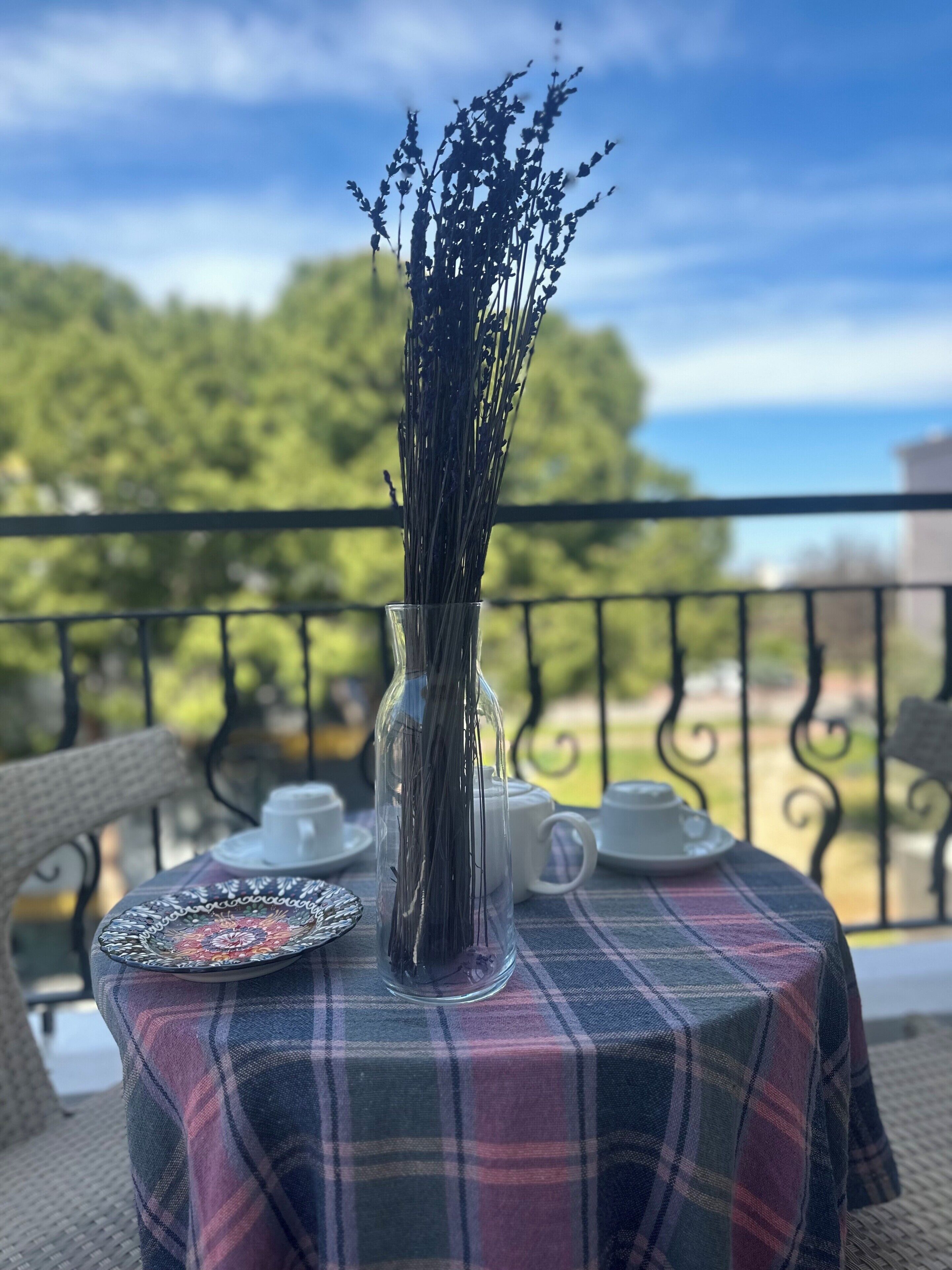 A table with a plaid tablecloth, a clear vase with dried flowers, and white teacups and saucers.
