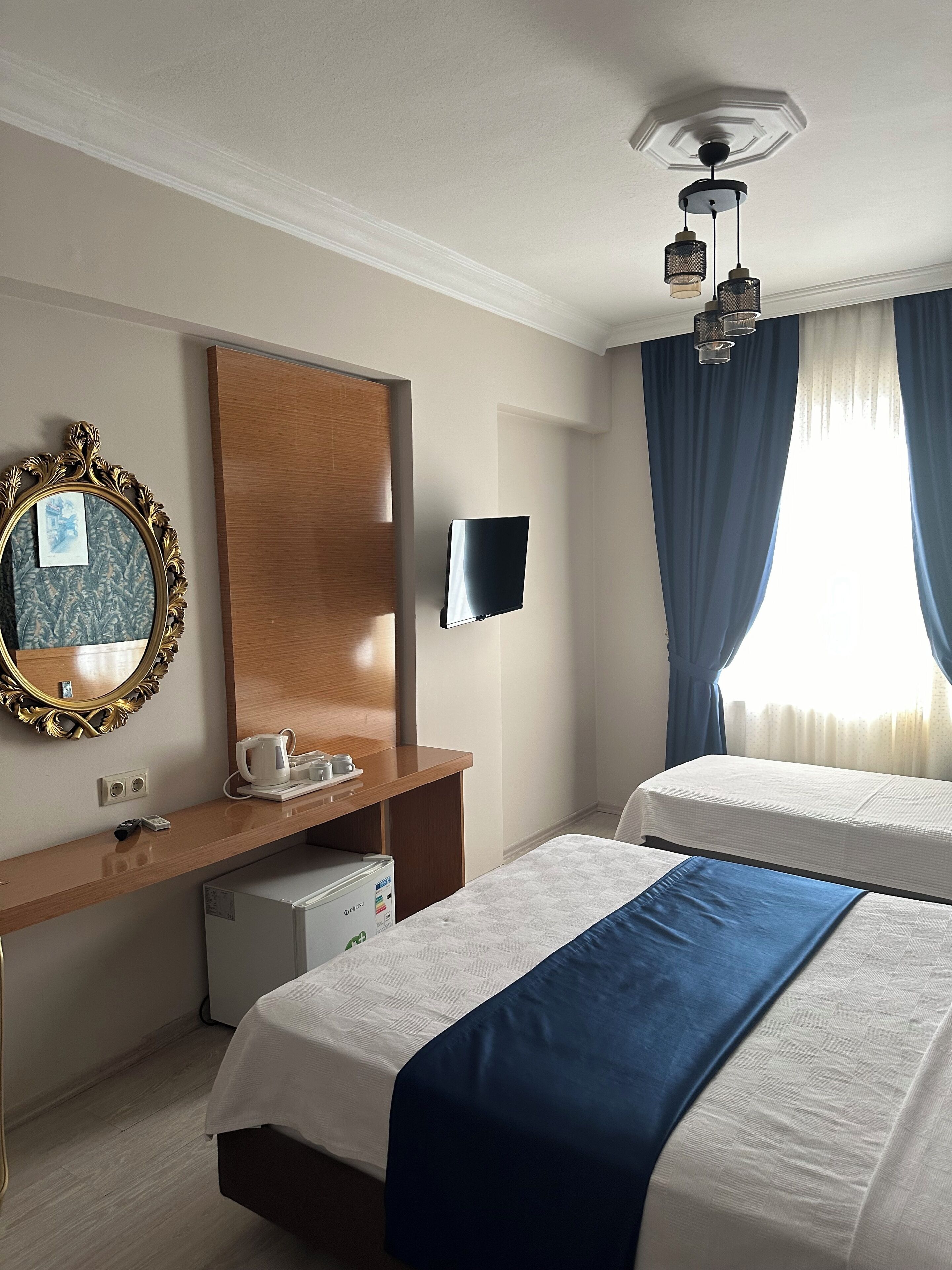 Une chambre d’hôtel avec deux lits, un bureau avec un miroir, une télévision et un luminaire au plafond.