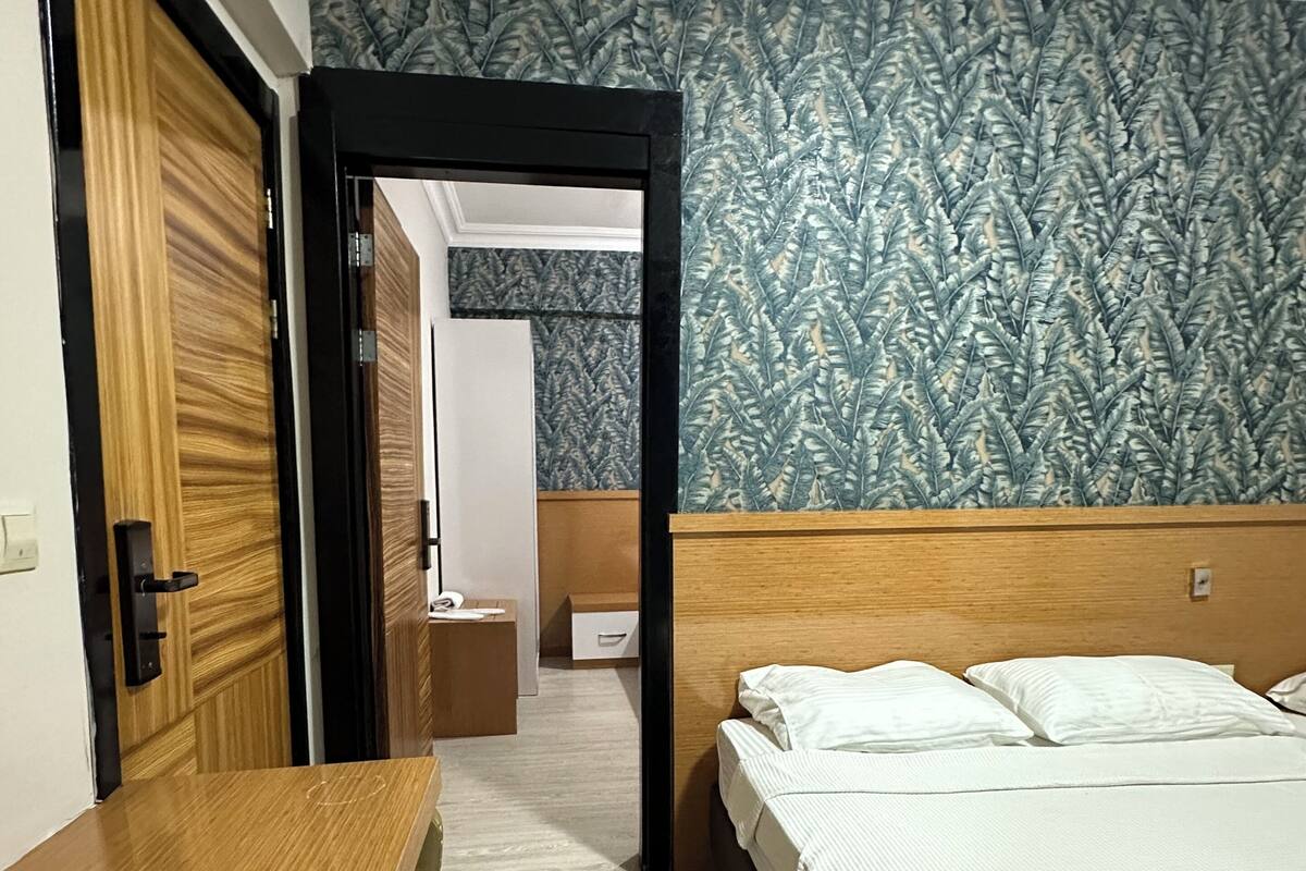 Une chambre d’hôtel avec un bureau en bois, un lit avec une literie blanche, un papier peint à motifs et une vue sur le couloir.