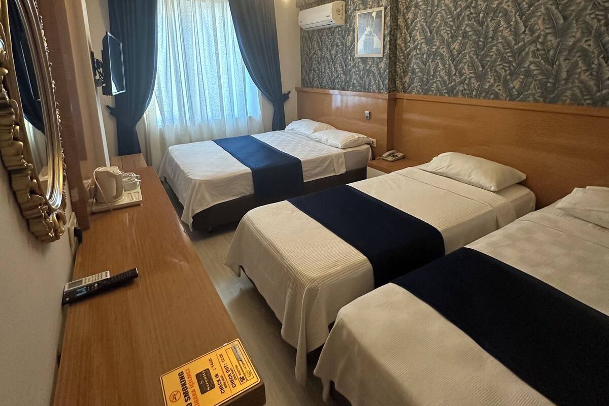 Une chambre d’hôtel avec deux lits, un bureau en bois, un miroir, un ventilateur de plafond et un mur décoré d’un motif.