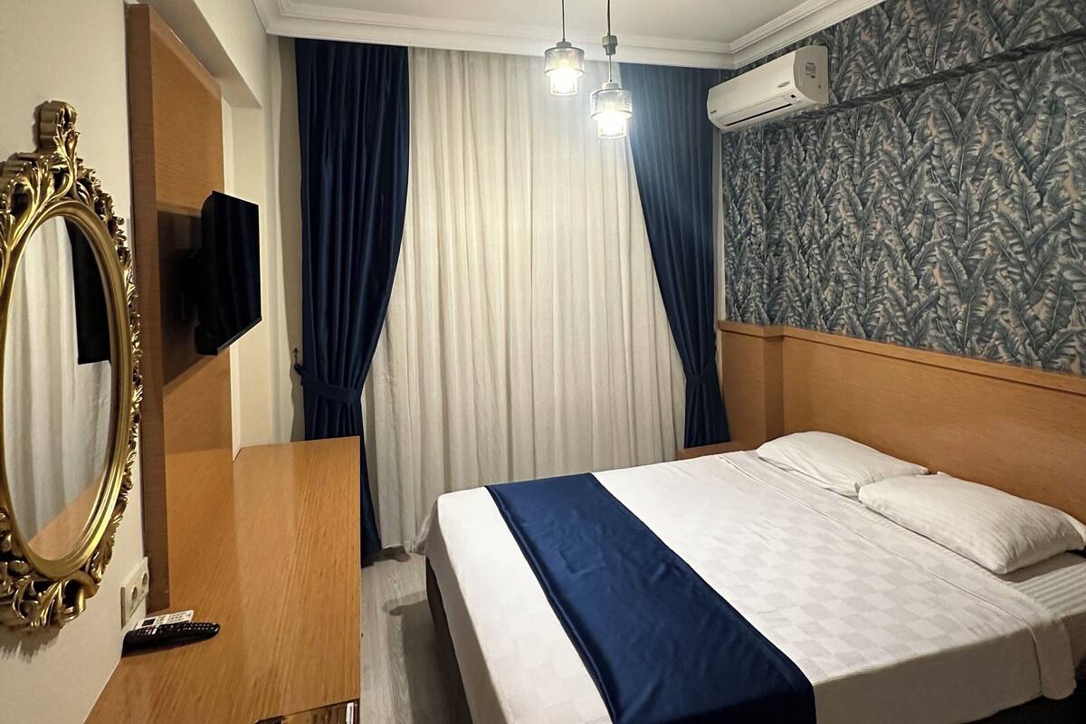 Une chambre d’hôtel comprenant un lit, un bureau en bois, un miroir, un luminaire au plafond et un appareil de climatisation.