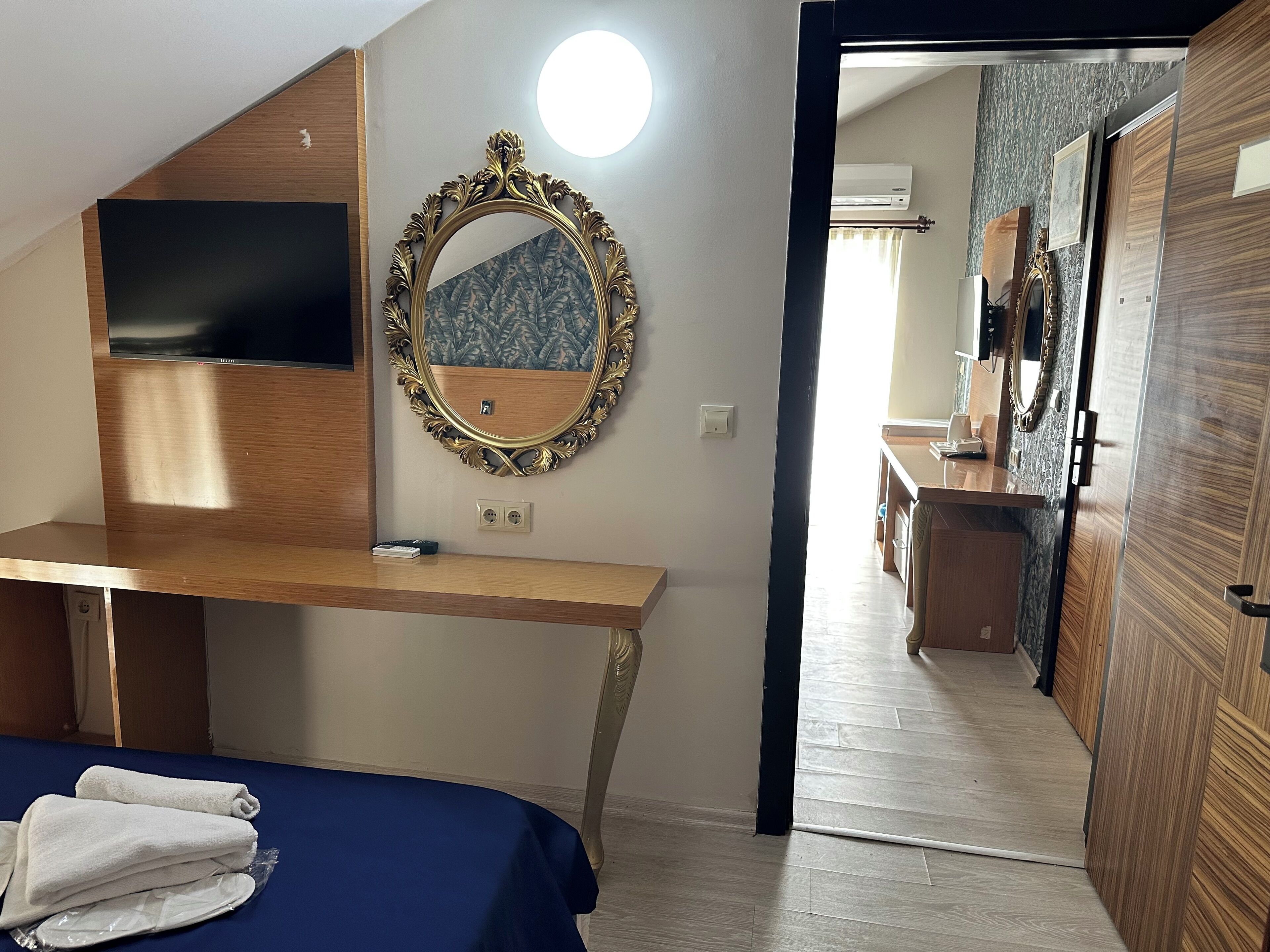 Una camera da letto con una scrivania in legno, un grande specchio, una televisione e un letto con asciugamani.