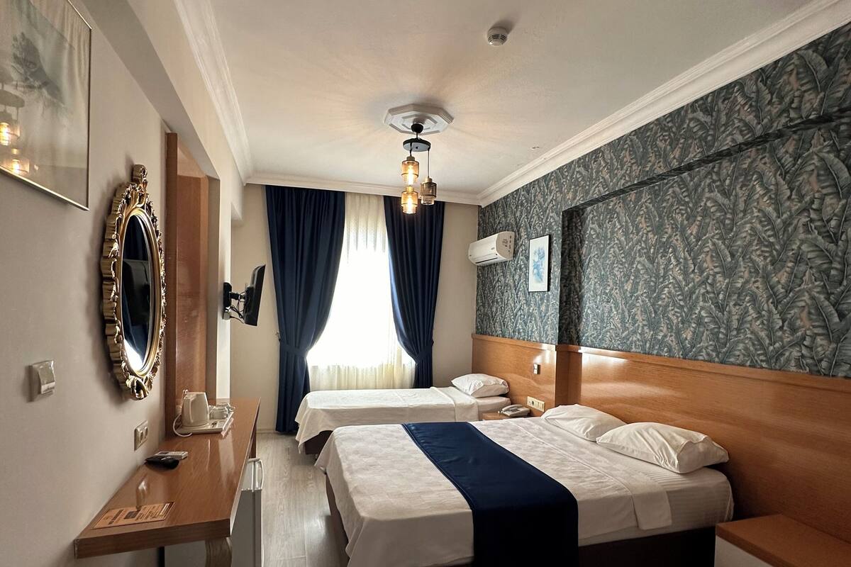 Une chambre d’hôtel avec deux lits, un bureau, un miroir et un ventilateur de plafond.