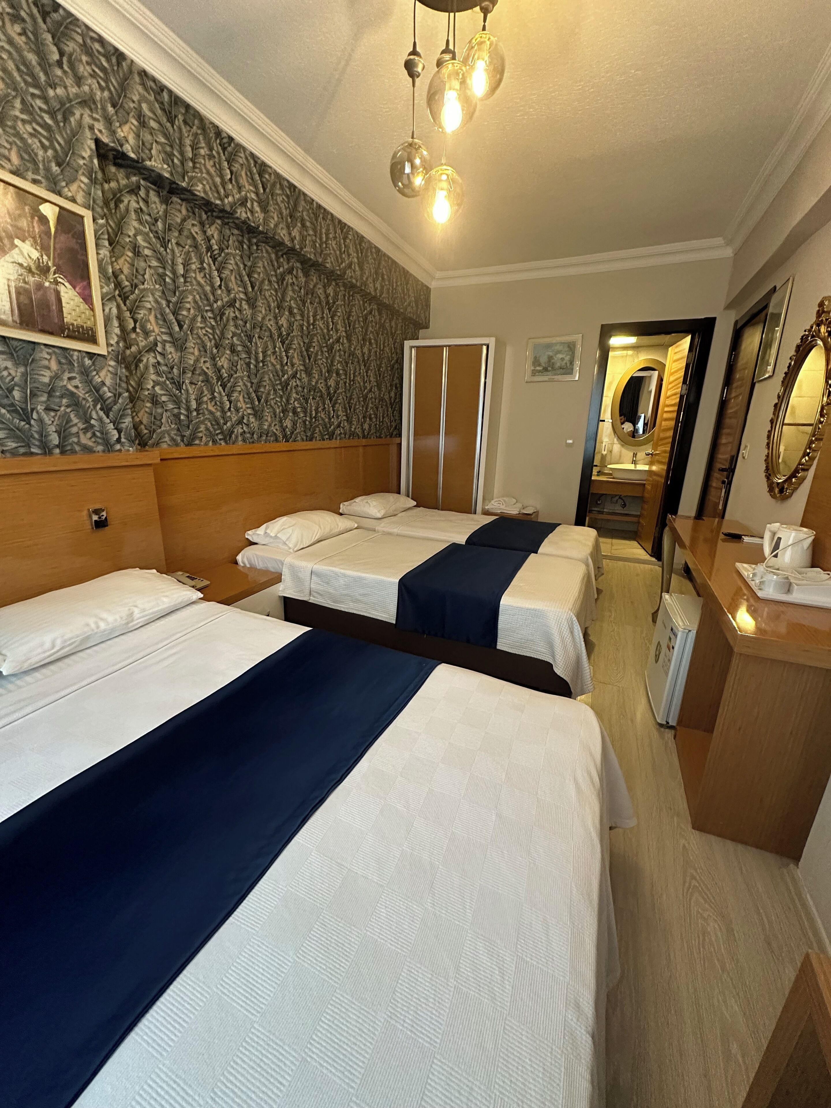 A hotel room with two beds, a wooden headboard, a mirror, a dresser, and a bathroom visible through an open door.