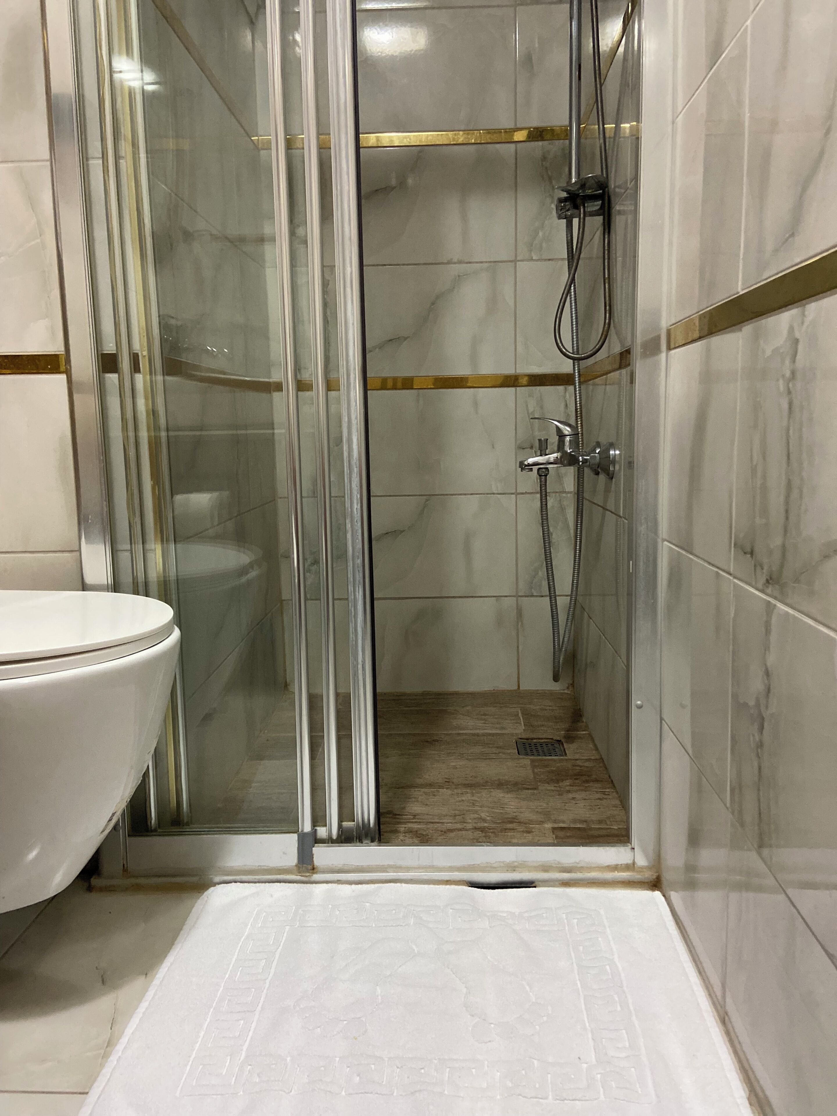 Un baño con ducha envuelta en vidrio, inodoro blanco y piso de mármol.