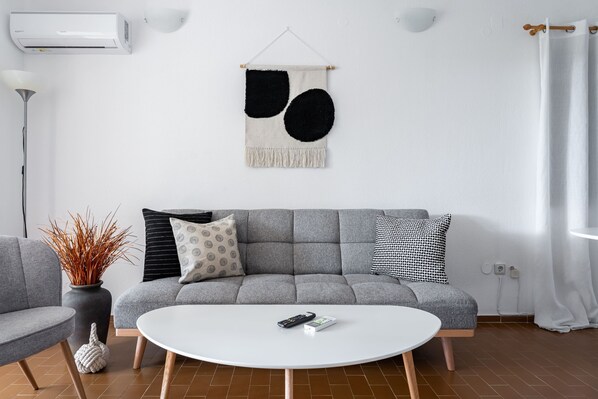 En moderne stue med en grå sofa, et hvidt sofabord og en vægmonteret aircondition.