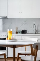 A modern kitchen with white cabinets, a marble backsplash, a stainless steel sink, and a wooden dining table with chairs.