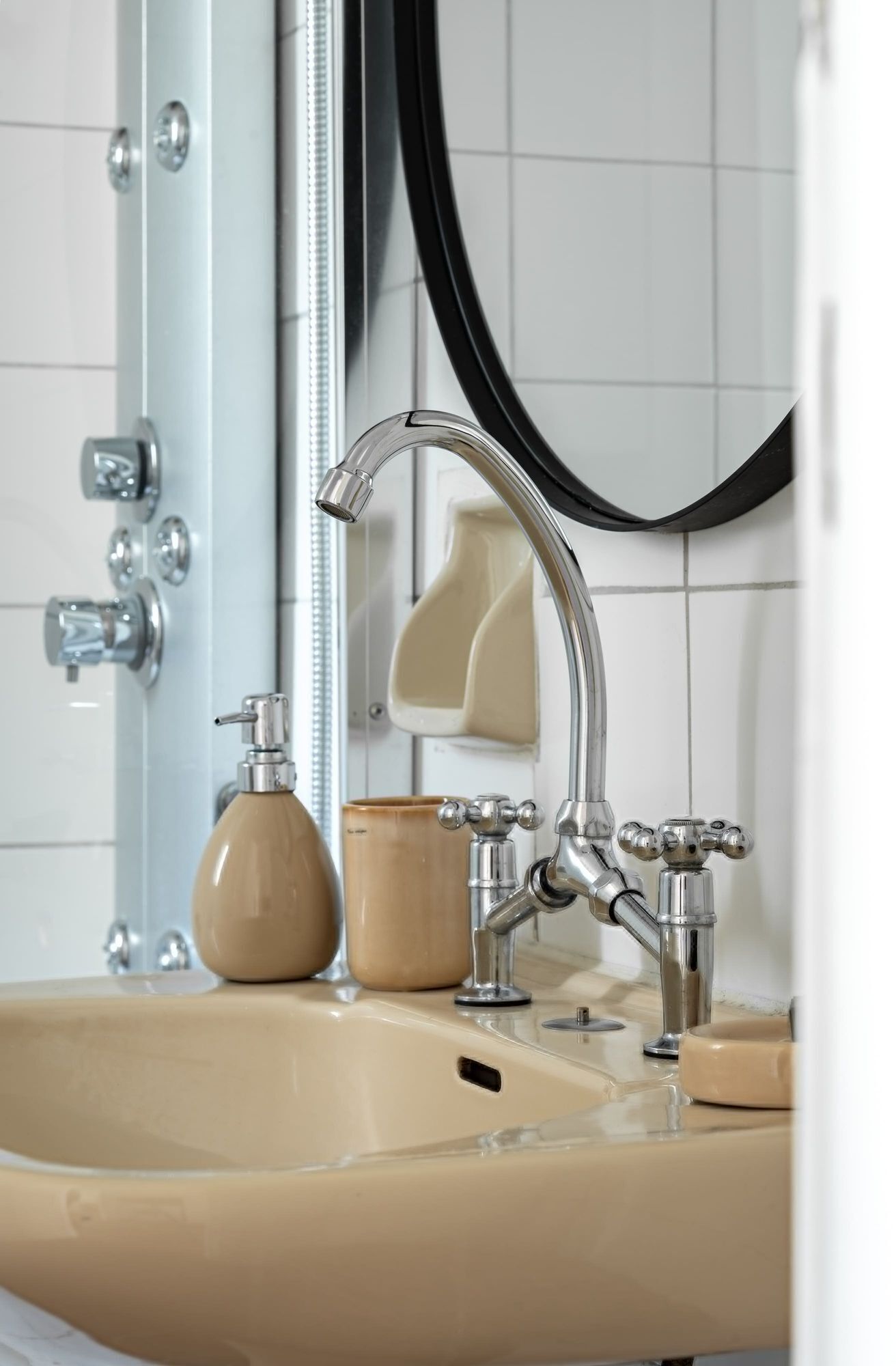 Une salle de bain équipée d’un lavabo, de deux robinets, d’un distributeur de savon et d’un miroir.