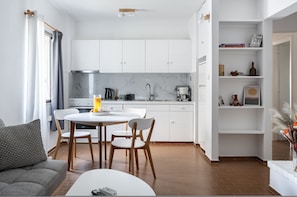 A modern kitchen with white cabinets, a dining table, and chairs. - Saronida Coastal Escape 2BR Apartment (Saronikos)