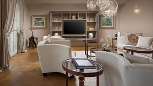 Uma sala de estar com uma televisão de tela plana grande, sofás brancos, uma mesa de centro de vidro e objetos decorativos nas estantes.