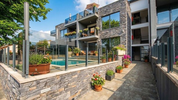 A modern multi-story building with a glass-enclosed pool, stone facade, and outdoor seating areas. - Comfortable Apartment Amore near Poreč with Balcony for 4 Guests (Kufci)