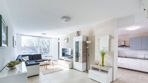 A modern living room with a sofa, TV, and a dining area with a kitchen in the background. - Comfortable Apartment Amore near Poreč with Balcony for 4 Guests (Kufci)
