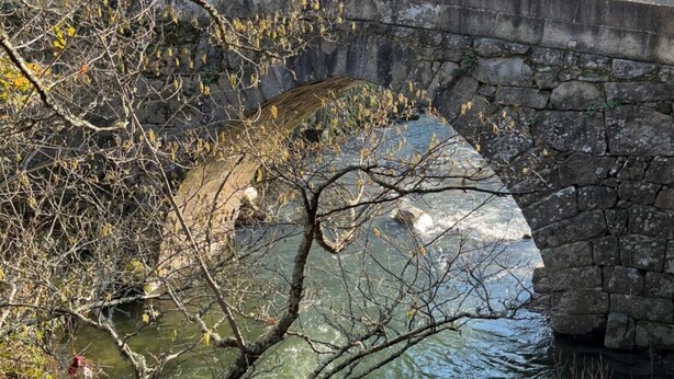 Un pont de pierre enjambant une étendue d’eau, avec une rambarde rouge au premier plan.