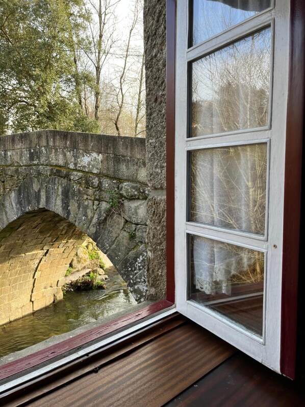 Un puente de piedra sobre un canal de agua, una ventana con vistas a árboles y un suelo de madera.