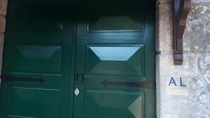 Une porte à deux battants, peinte en vert, avec une poignée en métal, et une petite plaque métallique portant les lettres « AL », fixée au mur sur la droite.