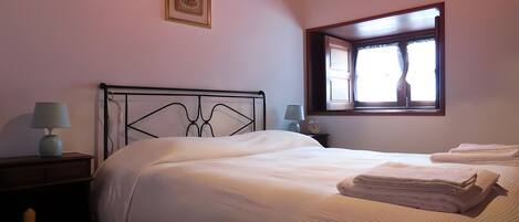 Un dormitorio con una cama, dos mesitas de noche con lámparas, una ventana con cortinas y un cuadro en la pared.