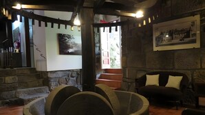 Une pièce aux murs de pierre, avec un puits en pierre, un escalier en bois, un canapé et un tableau encadré accroché au mur.