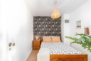 A bedroom with a patterned wallpaper, a bedside table with a lamp, a bed with patterned bedding, and a hanging light fixture. - Casa da Quelha - Douro (Marmelal)