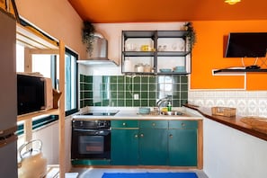 A compact kitchen with teal cabinets, a black oven, and a microwave. - Casa da Quelha - Douro (Marmelal)