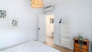 Ein Schlafzimmer mit einem Bett, einer Korbschaukel-Pendelleuchte, einer Klimaanlage, einer weißen Tür, einem weißen Kleiderschrank und einer kleinen Pflanze.