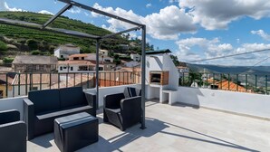 Eine Dachterrasse mit Gartenmöbeln, einer Pergola und Blick auf ein Dorf am Hang.