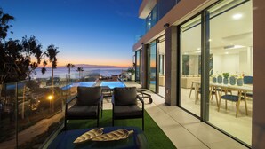 En moderne udendørs terrasse med pool, siddepladser og havudsigt i skumringen.