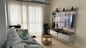 A living room with a sofa, TV, and a small side table. - Spacious apartment 160m from the beach, 3 bedrooms, barbecue. (Itapema)