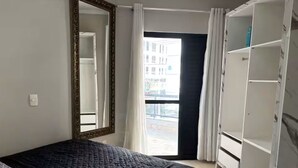 A bedroom with a bed, a wardrobe, a mirror, and a view of the outside. - Spacious apartment 160m from the beach, 3 bedrooms, barbecue. (Itapema)