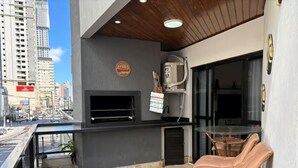 A rooftop terrace with a grill, seating, and a city view. - Spacious apartment 160m from the beach, 3 bedrooms, barbecue. (Itapema)