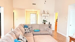 Un salón amplio con un sofá modular, un ventilador de techo y un estante decorativo.
