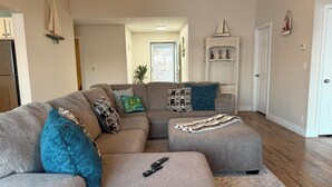 Una sala de estar con un sofá seccional, un reposapiés y un control remoto sobre el reposapiés.