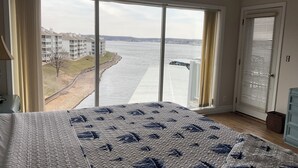 Un dormitorio con una cama grande, vistas a un cuerpo de agua y una puerta con persianas.
