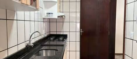 A kitchen with a sink, cabinets, and a door.