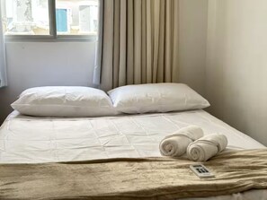Ein Bett mit weißer Bettwäsche, einer beigen Decke und aufgerollten Handtüchern.