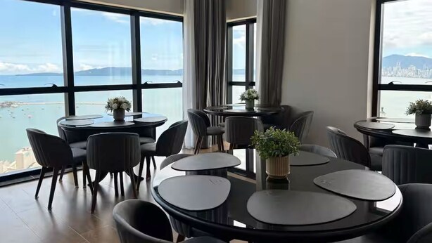 A modern dining area with round tables and chairs, large windows with a view of the sea and city skyline. - Apartment with Sea View • Comfort and Leisure in Itapema (Itapema)