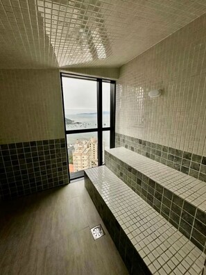 A bathroom with a tiled floor, a window with a view, and a bench. - Apartment with Sea View • Comfort and Leisure in Itapema (Itapema)