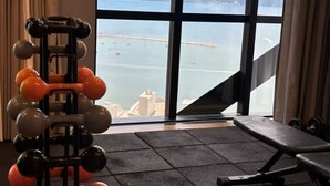 A gym with a weight rack, bench, and a view of the sea through large windows. - Apartment with Sea View • Comfort and Leisure in Itapema (Itapema)